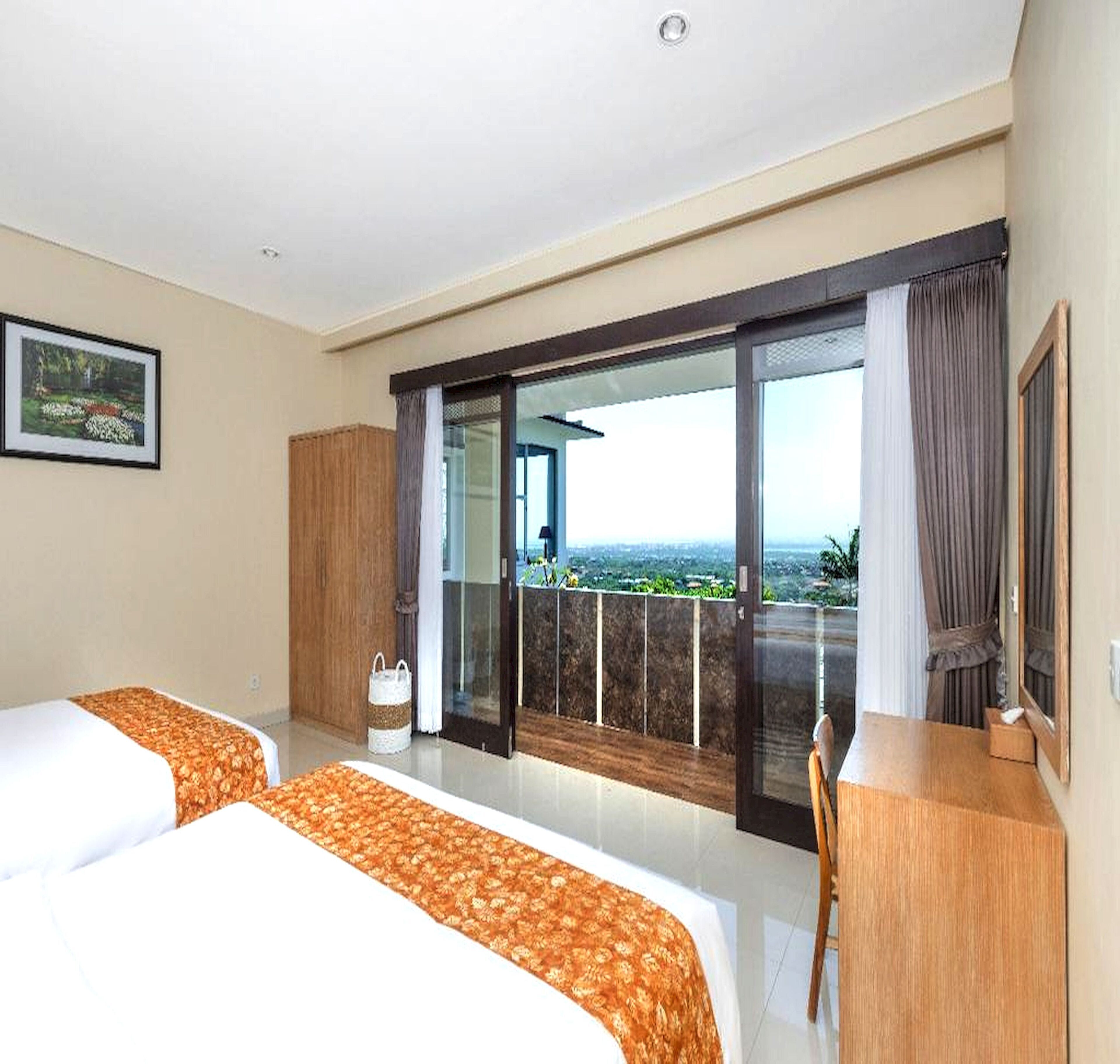 Une chambre d’hôtel avec deux lits, un bureau, une chaise, une grande fenêtre donnant sur un beau paysage et un tableau encadré au mur.
