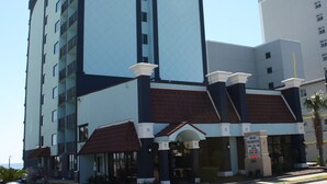 Ein mehrstöckiges Hotel mit modernem Design, das eine markante Eingangspforte mit Überdachung und einem Schild präsentiert.