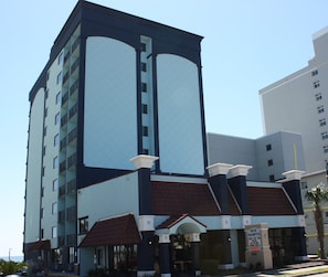 Een hotel met meerdere verdiepingen, uitgevoerd in modern design, met een opvallende entree met overdekt gedeelte en een naambord.