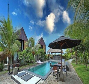 A pool area with lounge chairs and umbrellas, surrounded by palm trees and a clear sky. - Belvilla Seaside Hermitage Bungalow Canggu Beach (Nusa Dua)