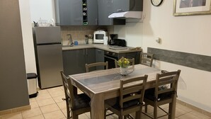 A compact kitchen with a dining table and chairs, a refrigerator, a microwave, and a clock on the wall. - Apparemment des Cèdres (Uzès)