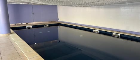 A swimming pool with a tiled floor, a blue wall, and a ceiling with a wave-like design.
