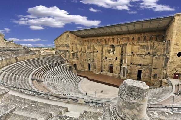 Un anfiteatro antiguo con asientos de piedra y un escenario central, rodeado de muros de piedra y un área cubierta.