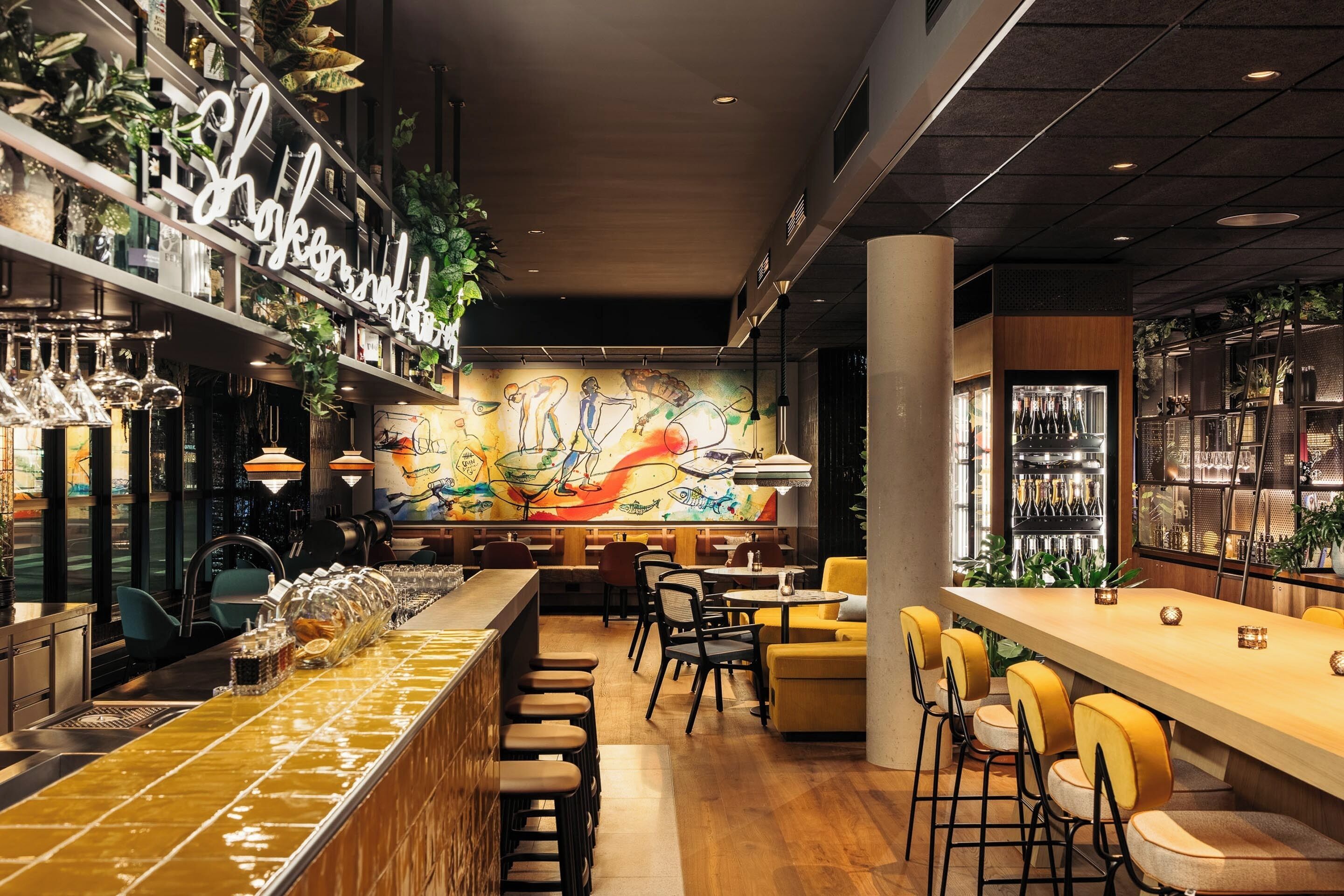 Un área de bar moderna con una barra larga, taburetes y un mural en la pared.