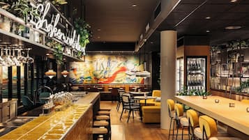 Un área de bar moderna con una barra larga, taburetes y un mural en la pared.