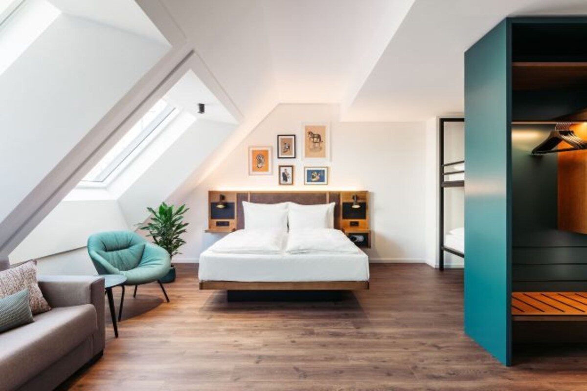 A modern bedroom with a skylight, a bed, a chair, and artwork on the wall.