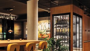 Een barruimte met houten vloer, barstoelen, een grote pilaar en een koelvitrine met flessen.