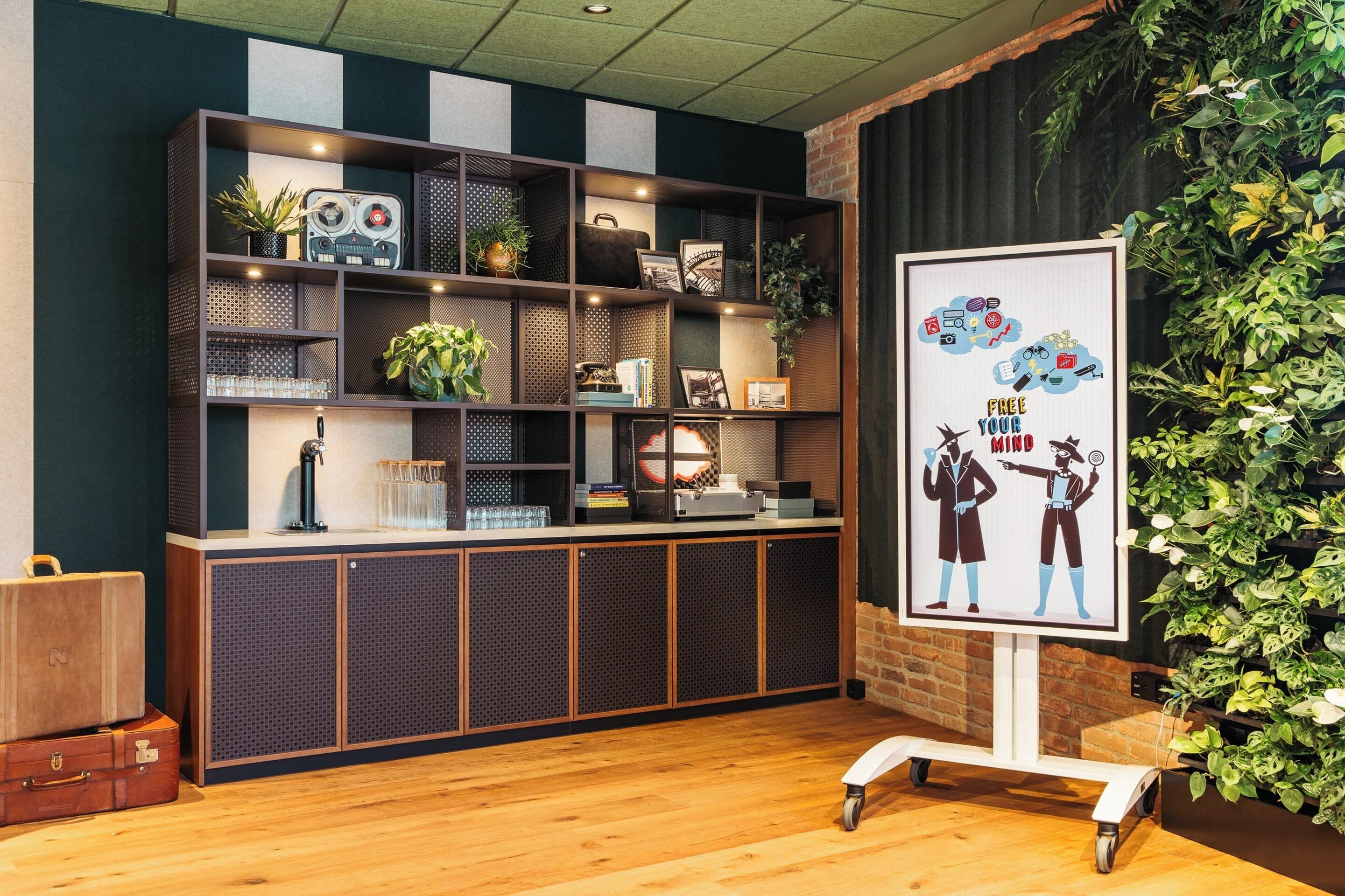 A reception area with a wooden desk, shelves with various items, a framed poster, and a green wall with plants.