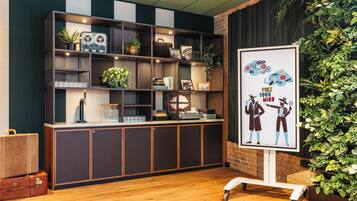 A reception area with a wooden desk, shelves with various items, a framed poster, and a green wall with plants.