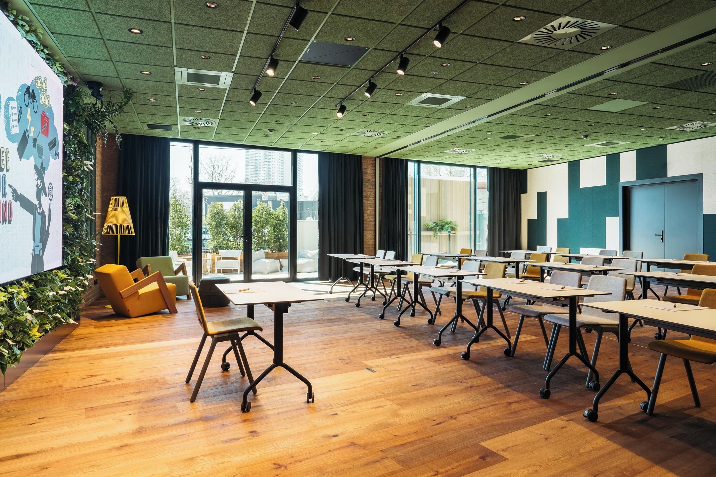 Una sala de conferencias moderna con suelo de madera, mesas y sillas, ventanas amplias y una pantalla de proyector.