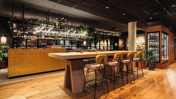 A modern bar area with a long counter, bar stools, and shelves stocked with bottles and plants.