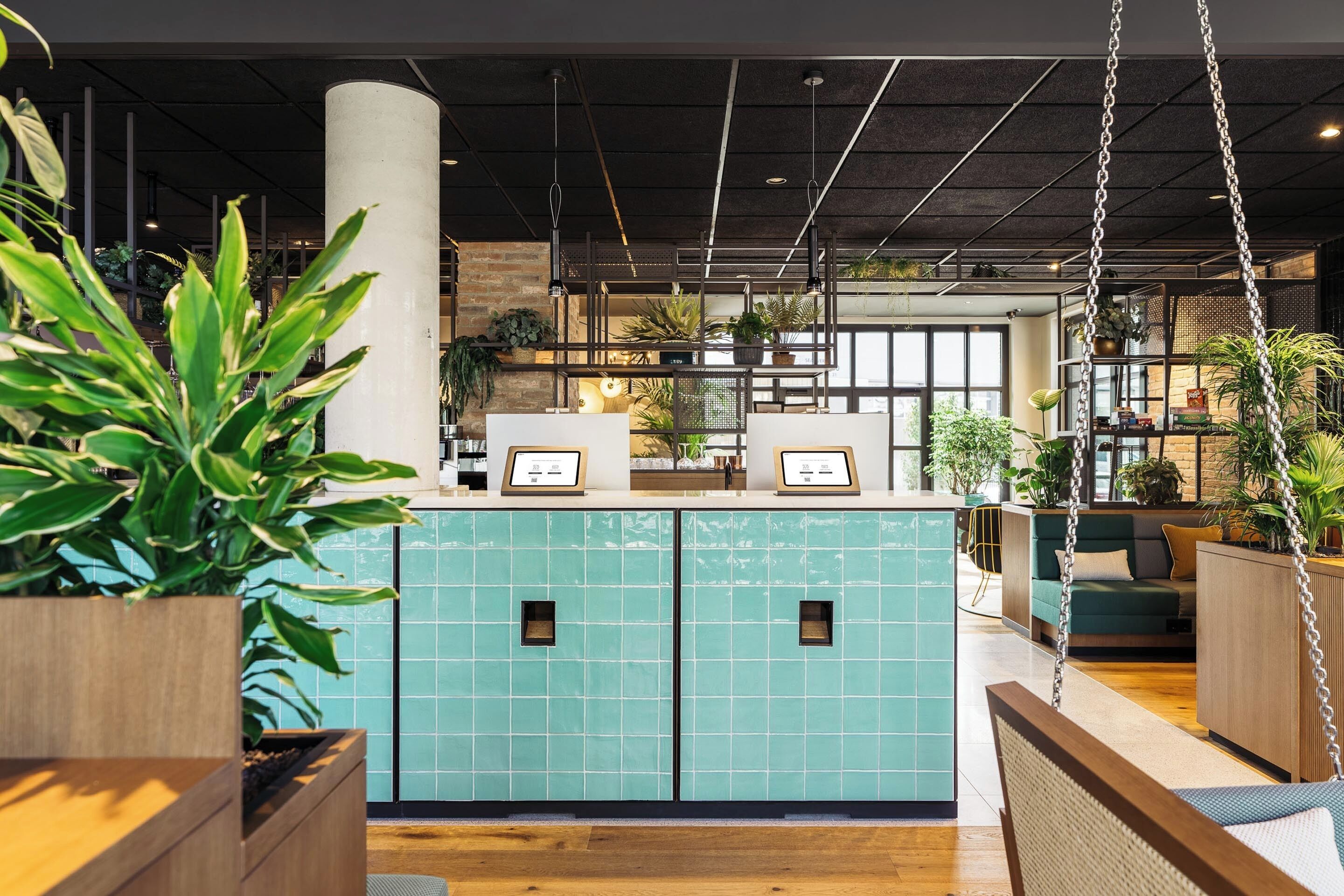Una moderna recepción con un mostrador de azulejos color turquesa, suelo de madera y plantas colgantes.