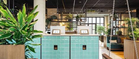 Una moderna recepción con un mostrador de azulejos color turquesa, suelo de madera y plantas colgantes.