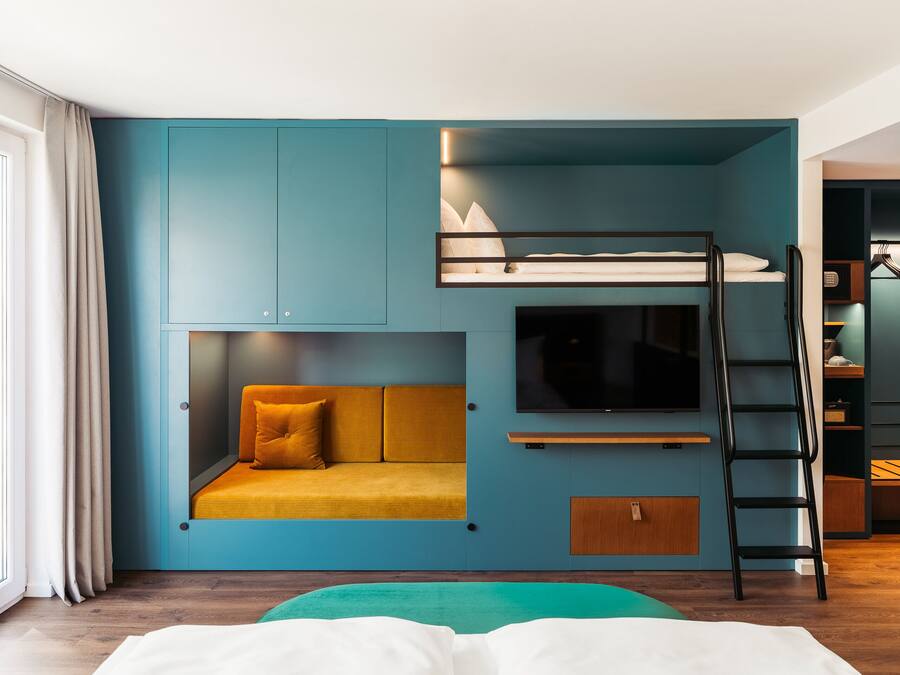 A modern room with a bunk bed, a sofa, a TV, and a ladder.