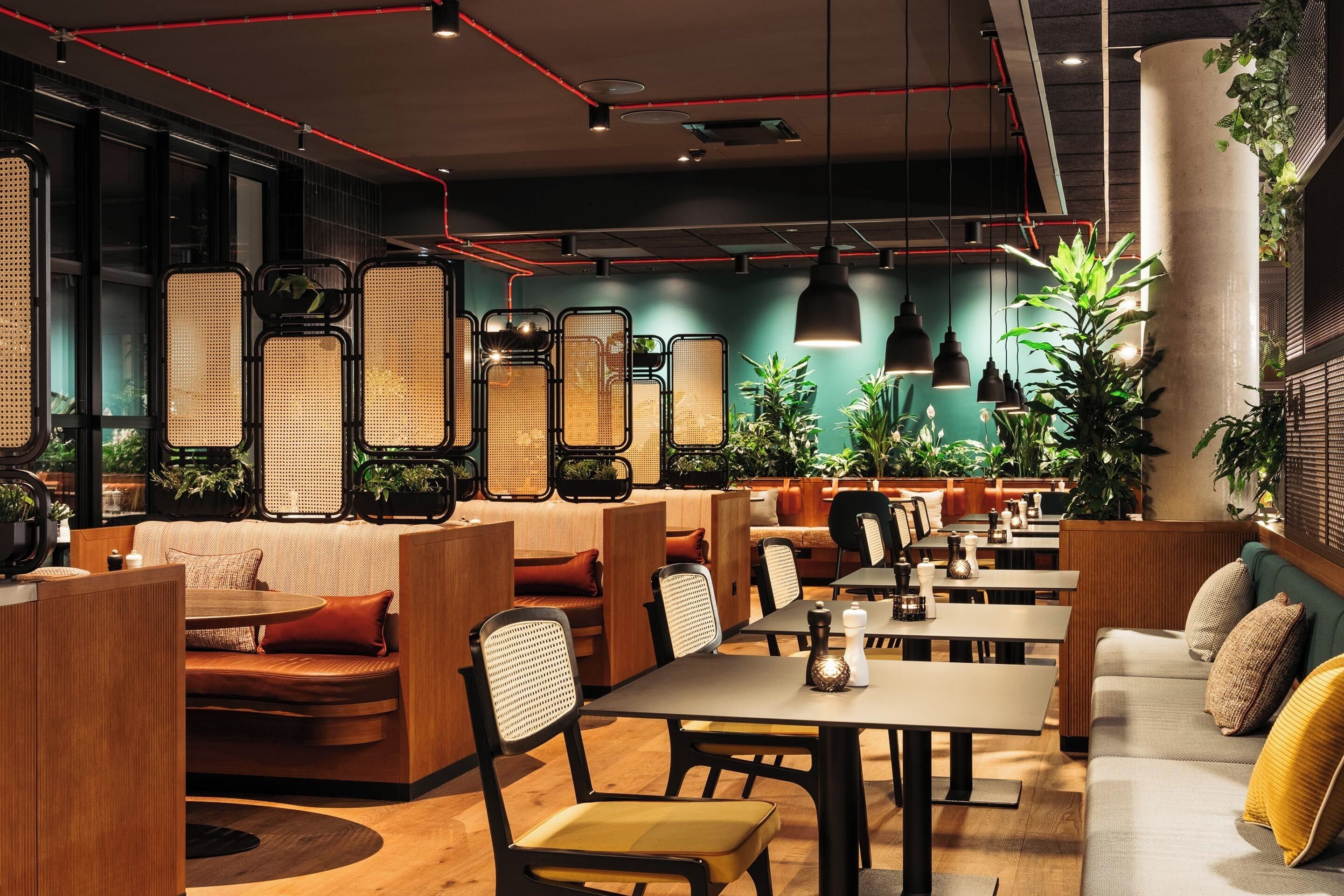 A modern restaurant interior with booths, tables, and hanging plants.