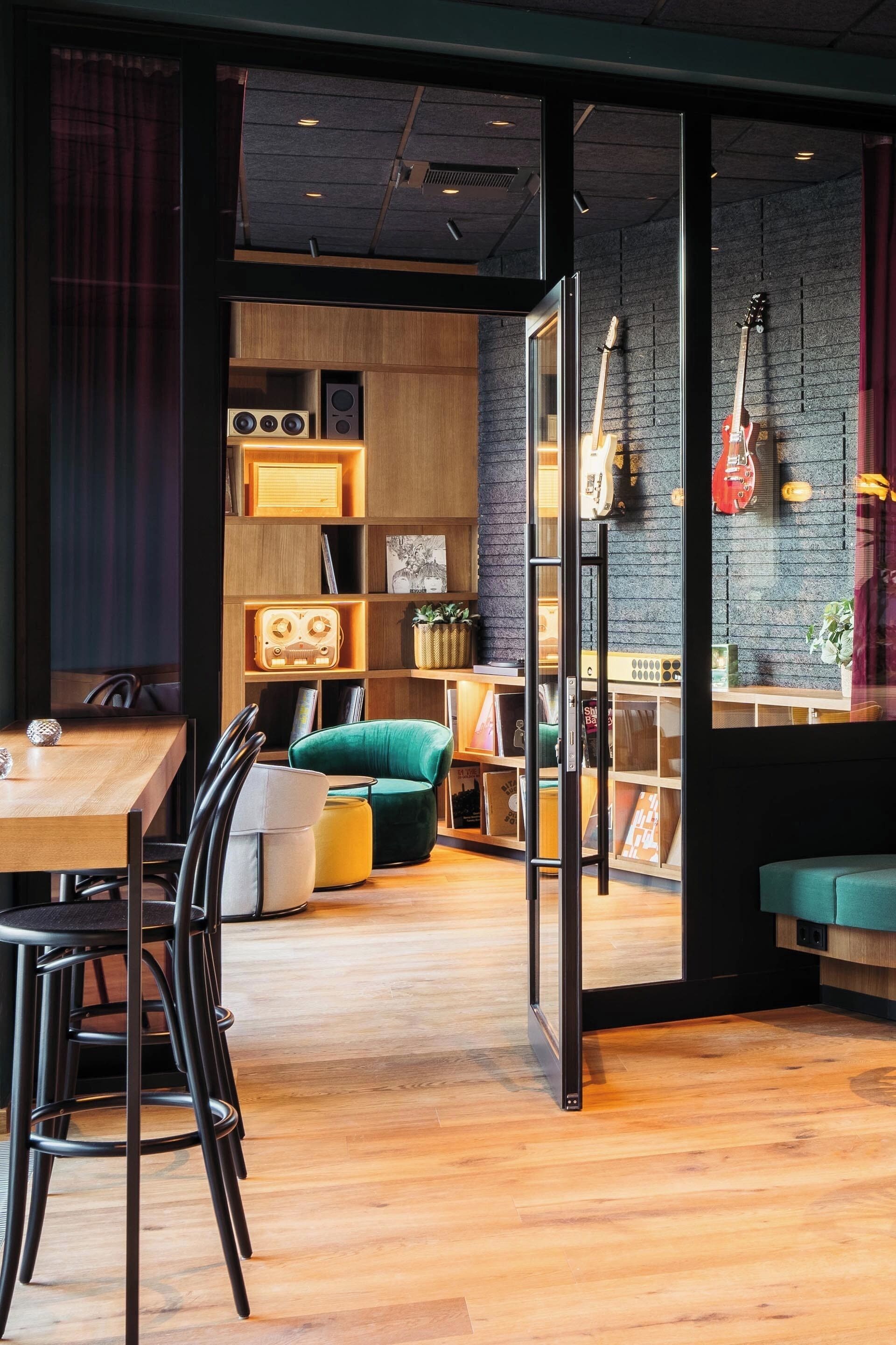 Un intérieur chaleureux avec une table en bois, des chaises, un canapé vert et une cloison en verre.