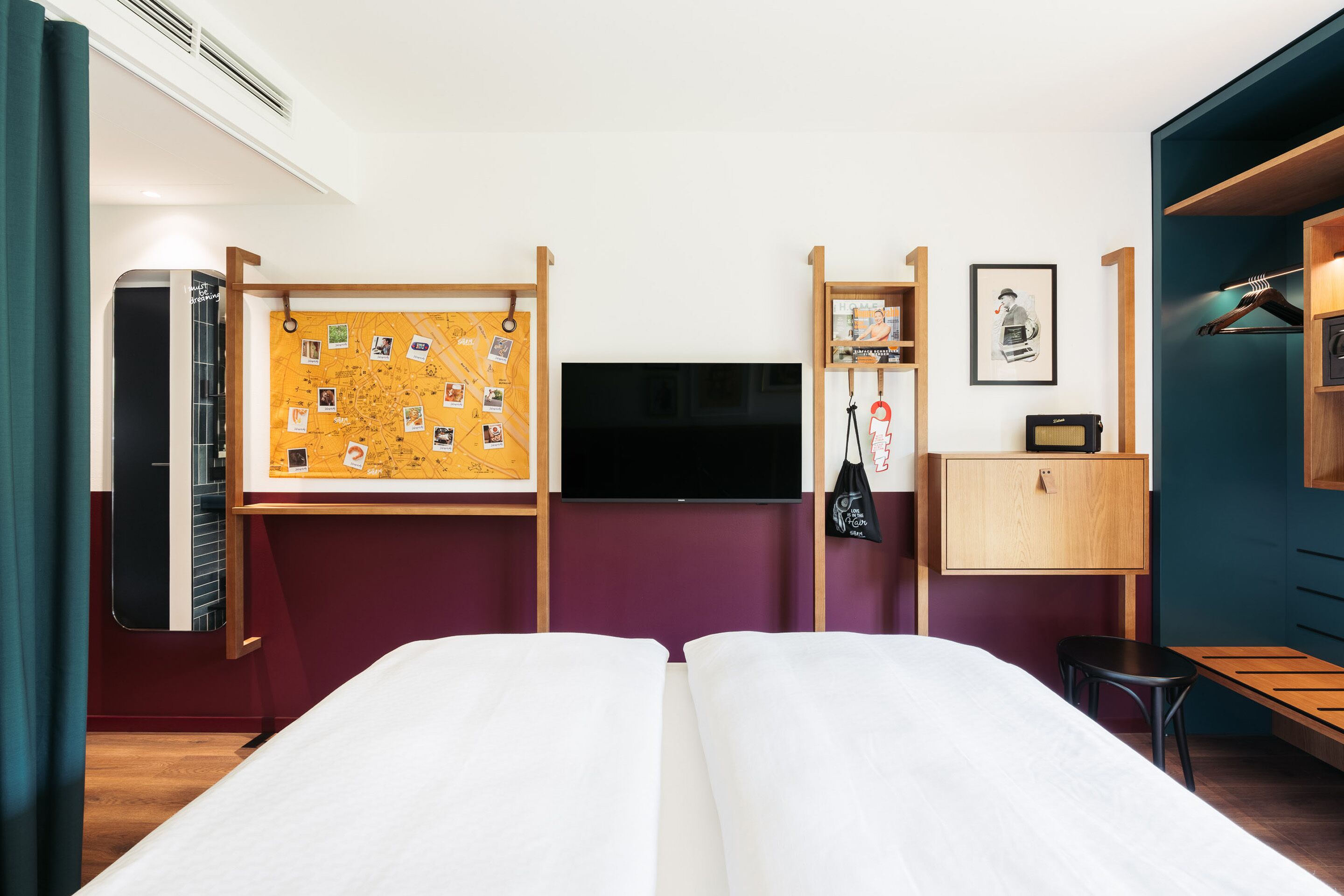 Ett hotellrum med två sängar, en TV, en anslagstavla med fotografier, ett skrivbord och en garderob.