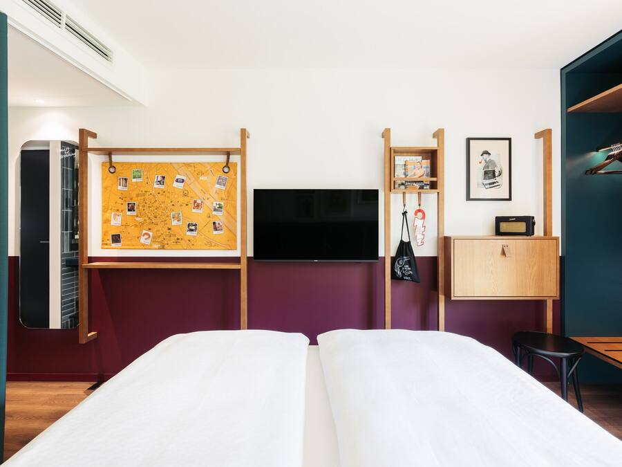 Habitación de hotel con dos camas, televisión, un tablón de corcho con fotos, escritorio y armario.