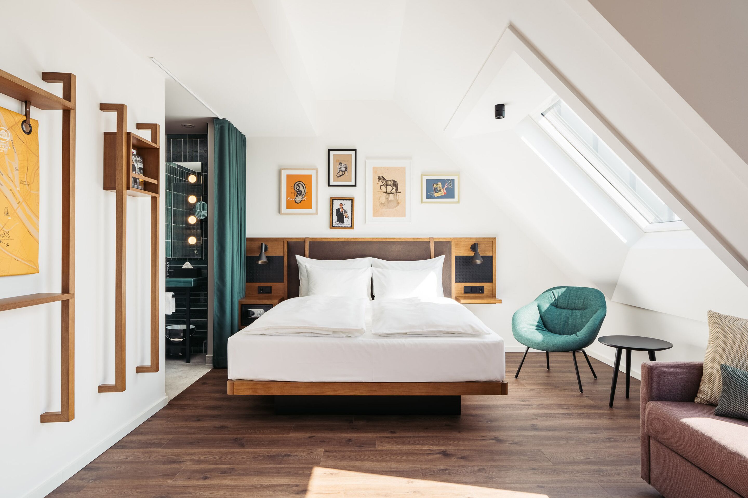 Camera moderna con un letto grande, un lucernario, una poltrona color petrolio e opere d'arte alle pareti.