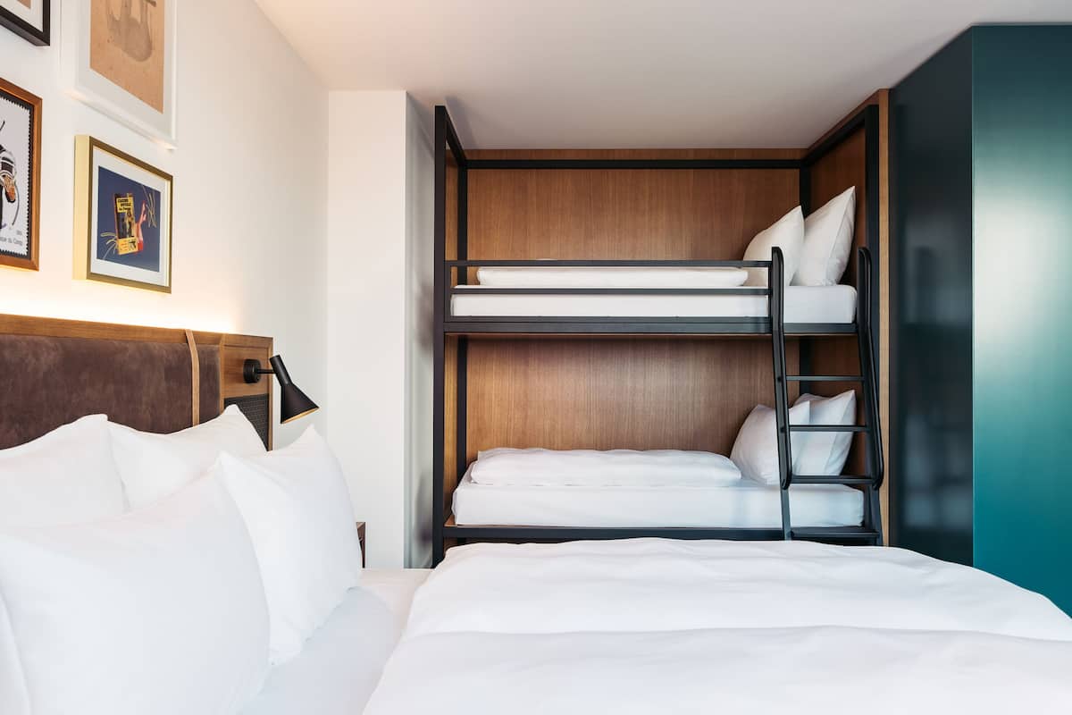 Ein Stockbett mit weißer Bettwäsche, einem Holz-Kopfteil und einer schwarzen Leiter.