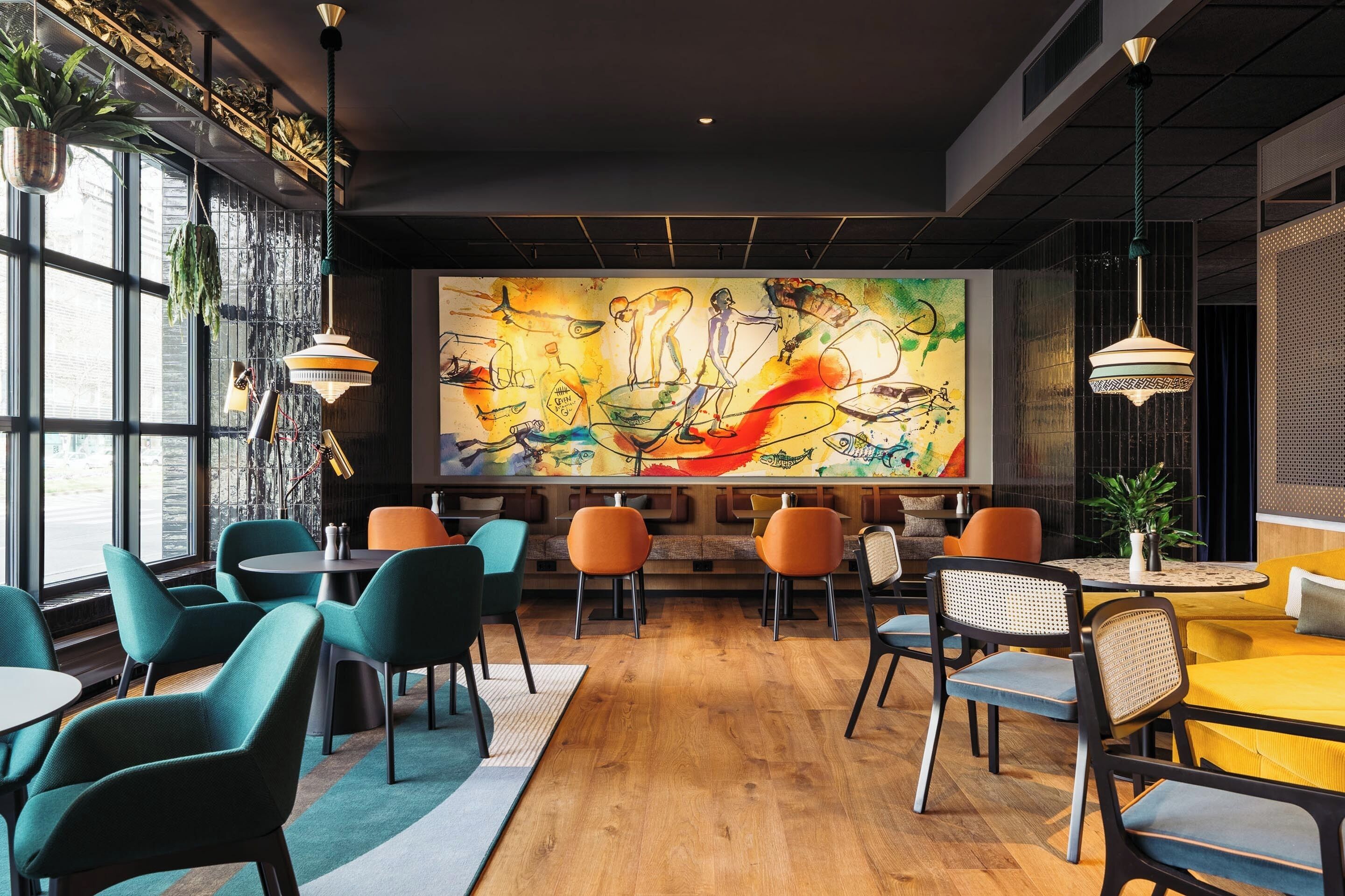 A modern cafe with a large mural, wooden flooring, and colorful chairs.