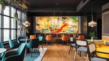 A modern cafe with a large mural, wooden flooring, and colorful chairs.
