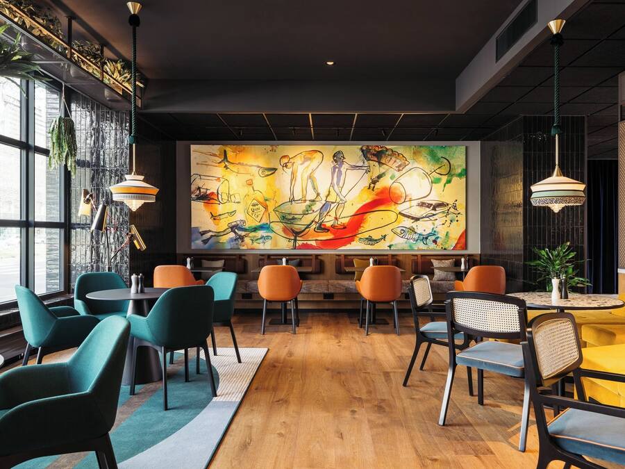 A modern cafe with a large mural, wooden flooring, and colorful chairs.