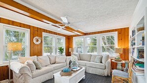 Una sala de estar acogedora con dos sofás beige, una mesa de centro blanca y un ventilador de techo.