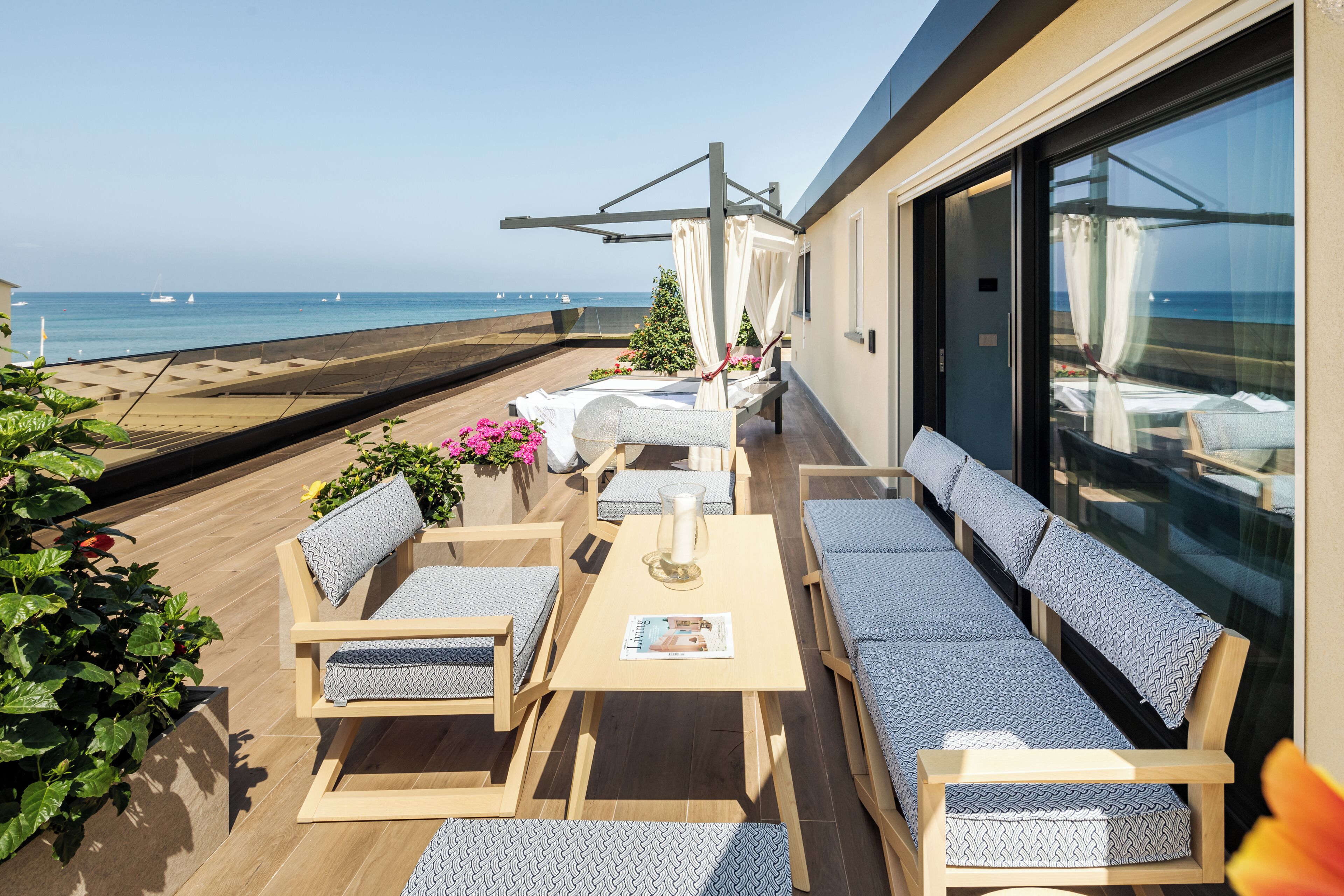 A sunlit outdoor seating area with wooden furniture and a view of the sea.