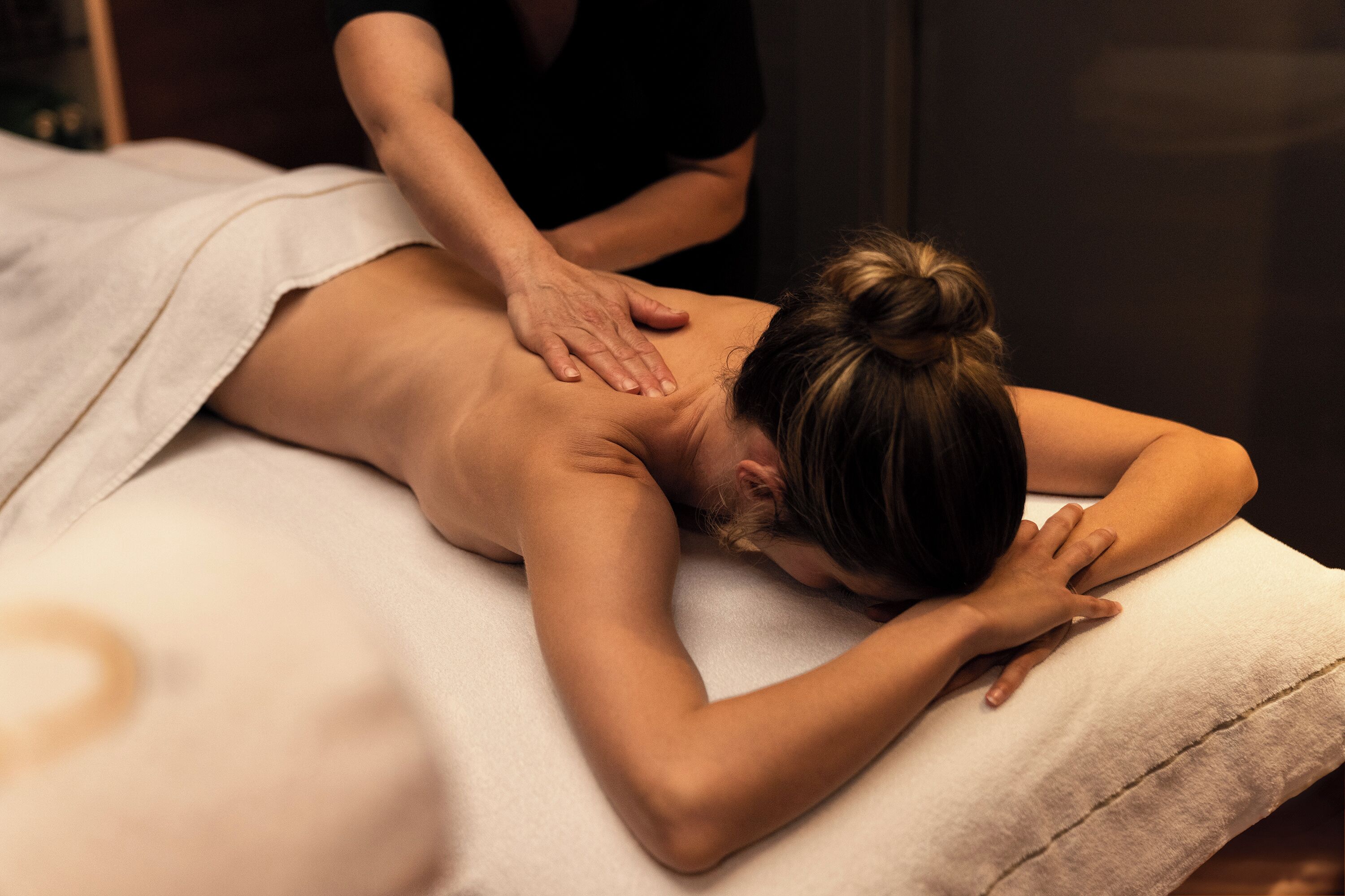 A person receiving a back massage in a room with a massage table and a plain wall in the background.
