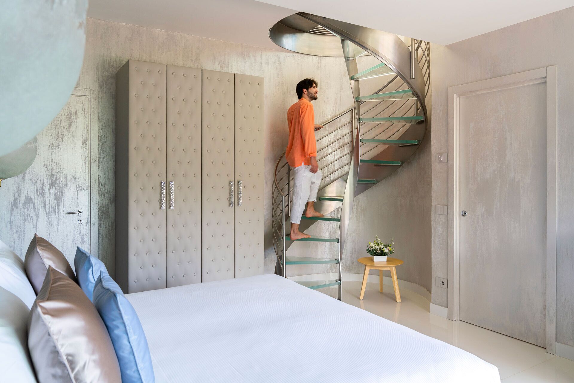 Une chambre avec un lit, une armoire, un escalier en colimaçon et une petite table sur laquelle est posée une plante.