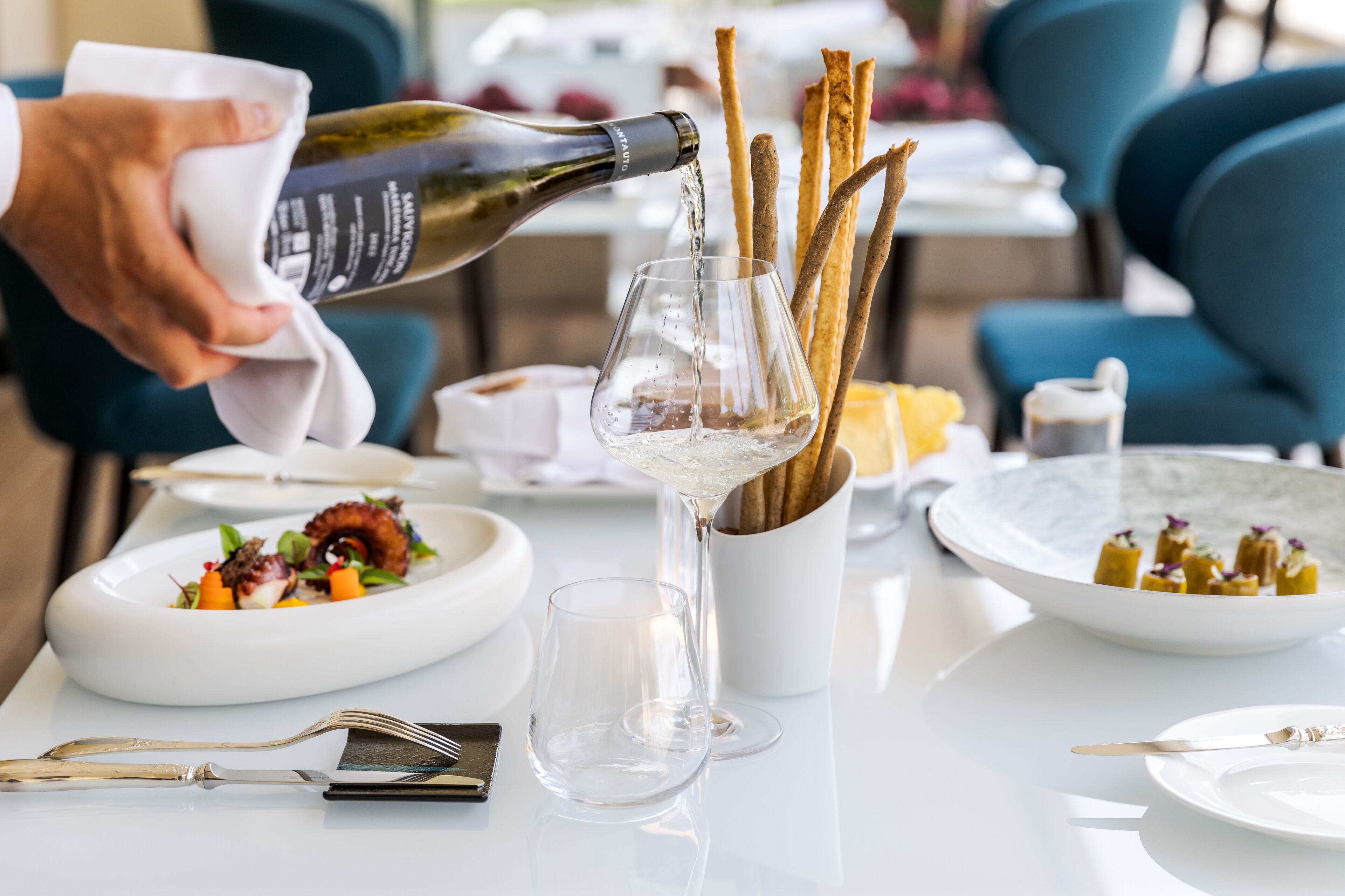A dining table with a bottle of wine being poured into a glass, surrounded by plates of food and cutlery.
