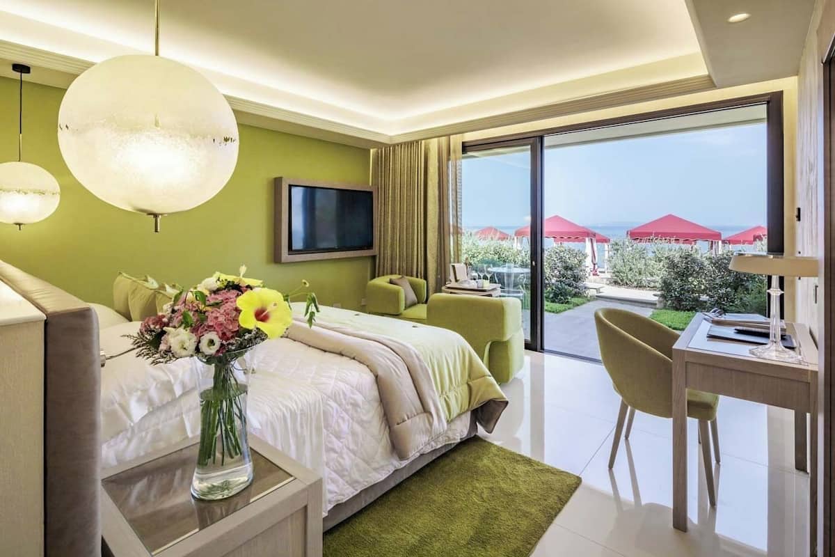 Una habitación de hotel moderna con cama, escritorio, silla, televisor y balcón con sombrillas rojas.