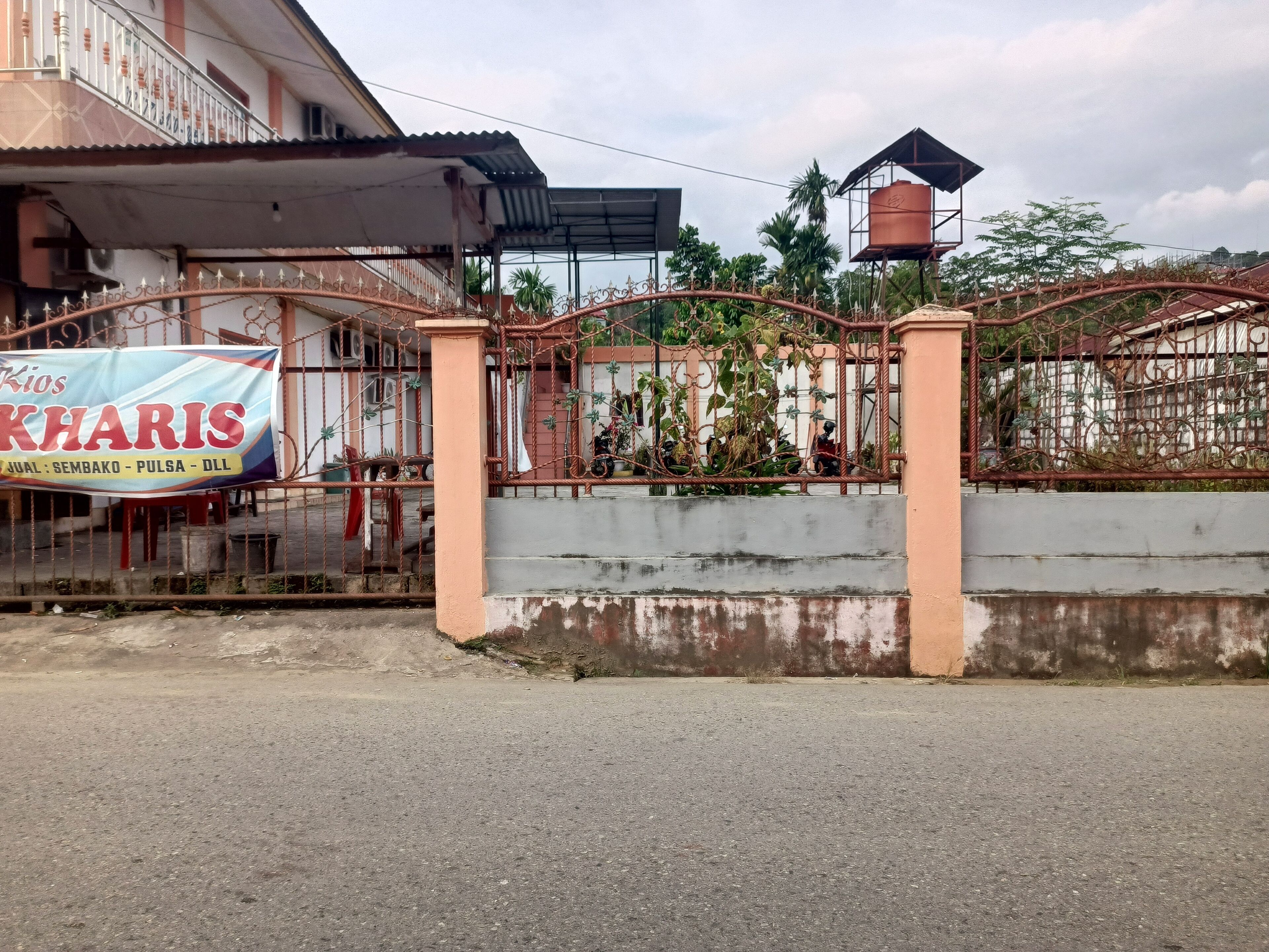 A gated entrance with a sign for 'Kios Kharis' and a metal fence.