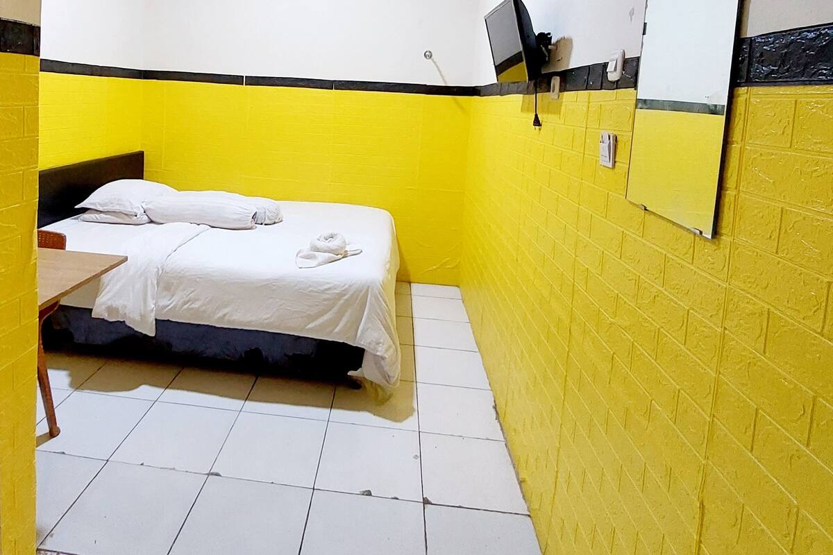 Una habitación pequeña y colorida con una cama, un televisor montado en la pared y un espejo.