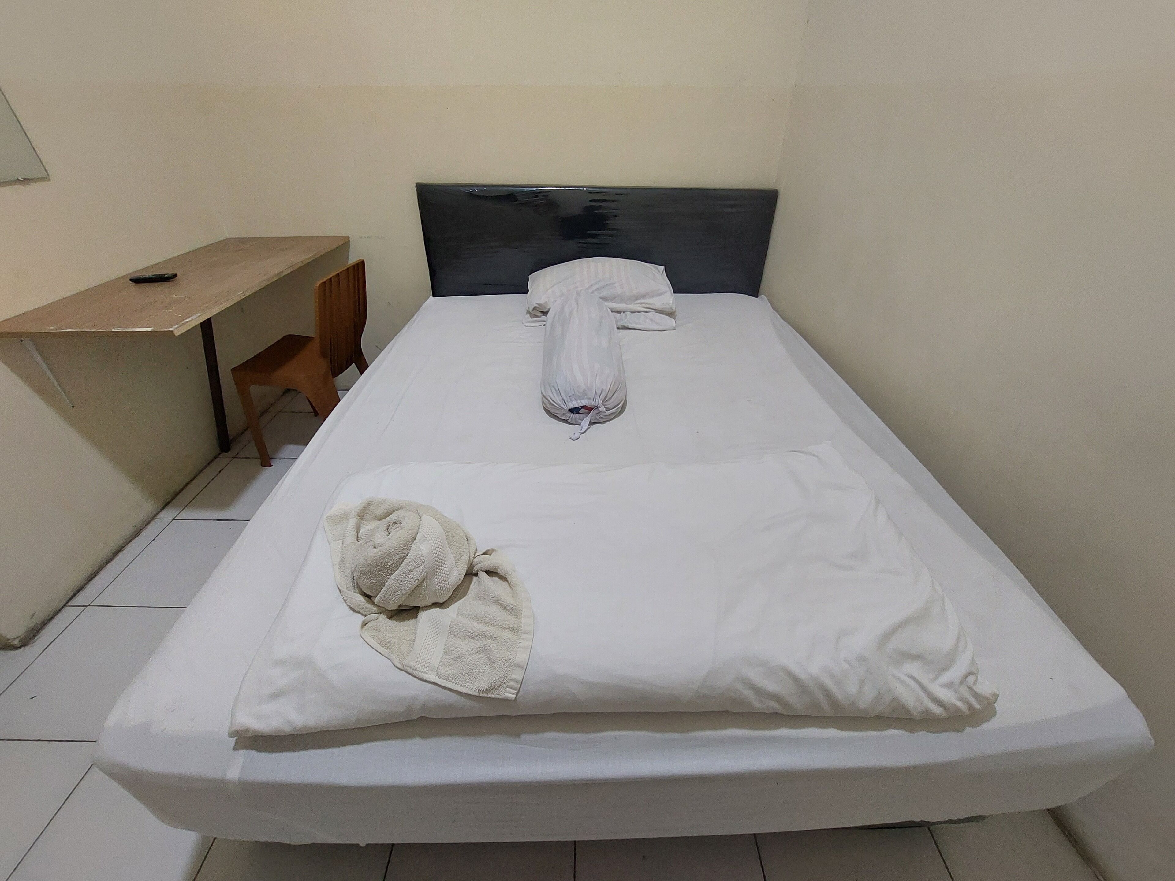 Un lit simple avec du linge de lit blanc, une tête de lit et un bureau en bois avec une chaise.