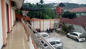 A balcony with a tiled floor, a metal railing, and a view of parked cars and buildings in the background.