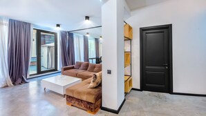 Un salon moderne avec un canapé d’angle, une table basse et une porte-fenêtre coulissante donnant sur un balcon.