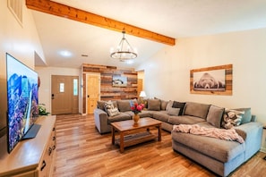 A living room with a wooden floor, a sofa set, a coffee table, and a TV. - Mountain View - PoolTable - Hot Tub - Huge Yard Pets (Sevierville)