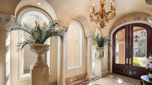 Un amplio vestíbulo con arquitectura clásica, que presenta arcos, un candelabro y plantas en macetas.