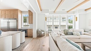 Een ruime woonkamer met een grote bank, een eettafel en een keuken met houten kasten en een roestvrijstalen koelkast.