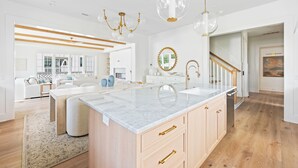 Een ruime keuken met een groot eiland, houten kasten en een moderne kroonluchter.