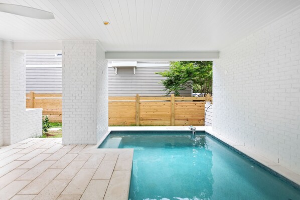 Una piscina interior moderna con paredes de ladrillo blanco y una valla de madera al fondo.