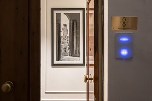 A door with a framed black and white photograph of a statue, a brass plaque with a fleur-de-lis symbol, and a blue illuminated control panel. - Residenza Quartieri Storici  (Florence)