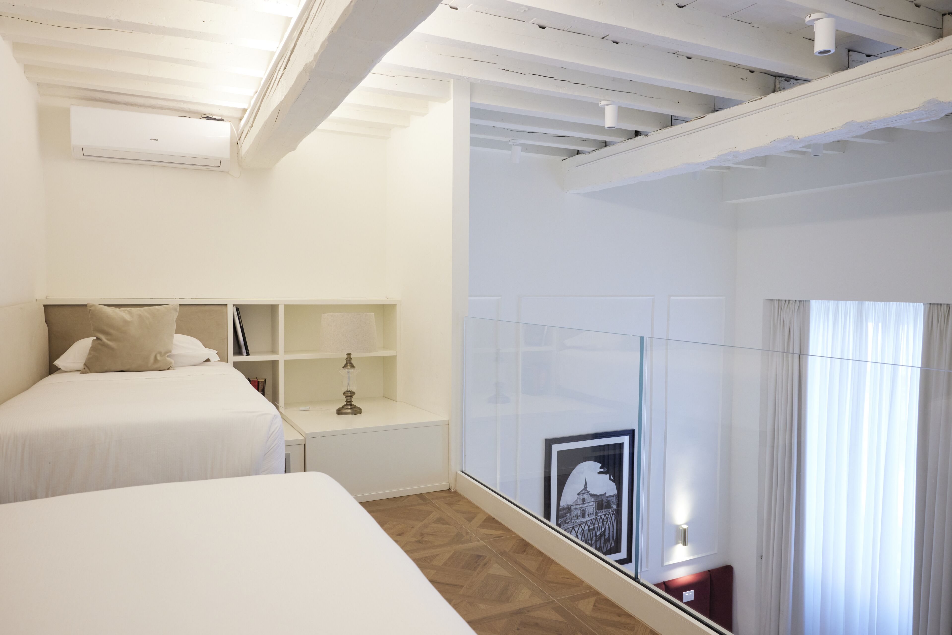 A bedroom with two beds, a nightstand, a lamp, a framed picture, and a window with curtains.