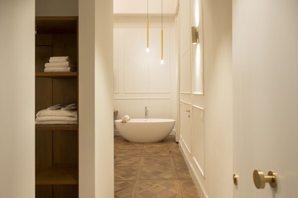 A modern bathroom with a freestanding bathtub, wooden shelving with towels, and pendant lighting.