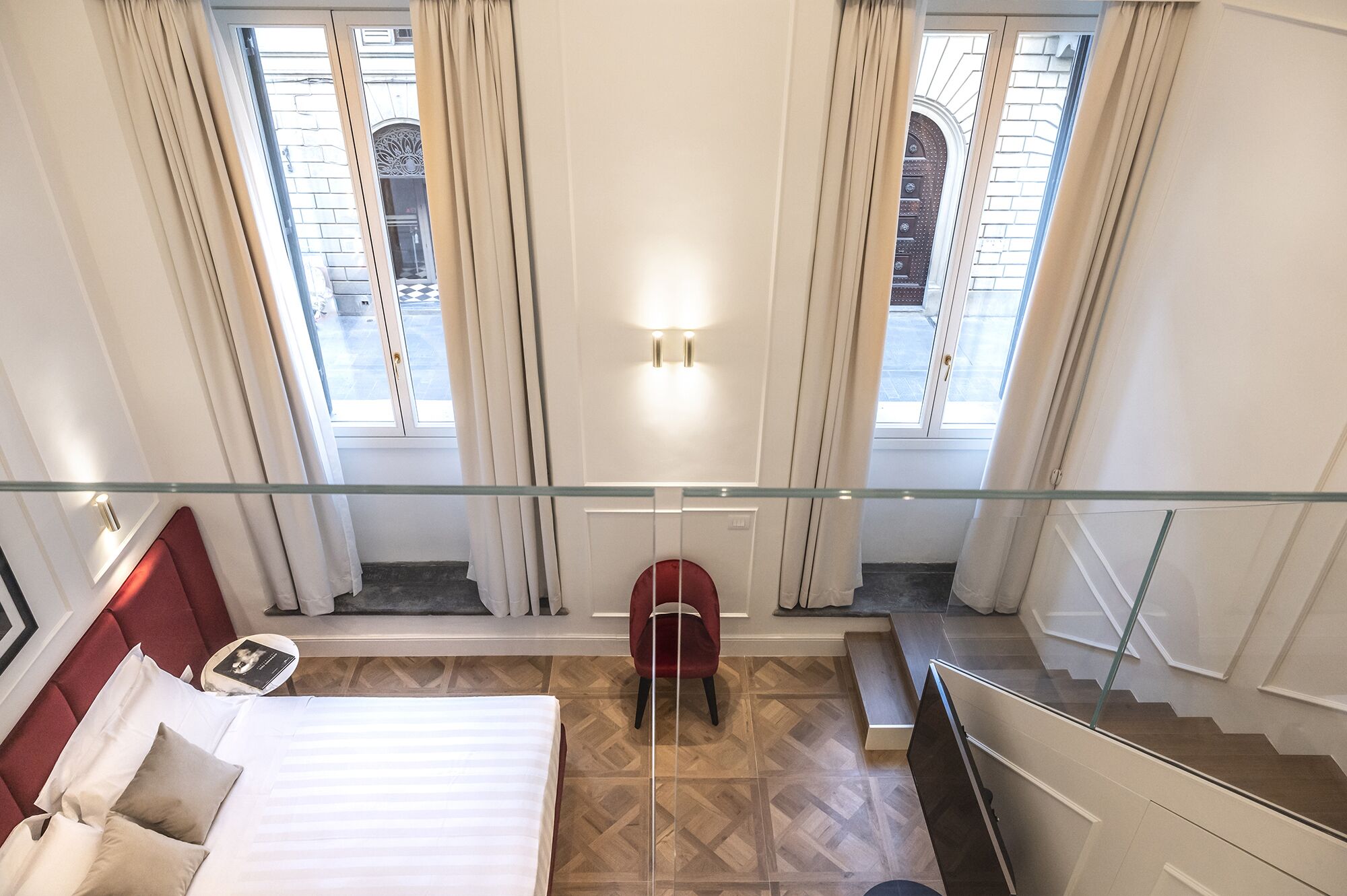 Een hotelkamer met een bed, een rode stoel, een glazen hekwerk en uitzicht naar buiten.