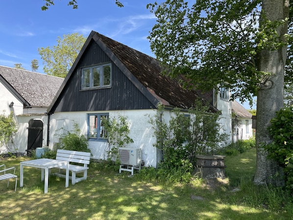A house with a sloped roof, a white exterior, and a small garden with a bench and an air conditioning unit.