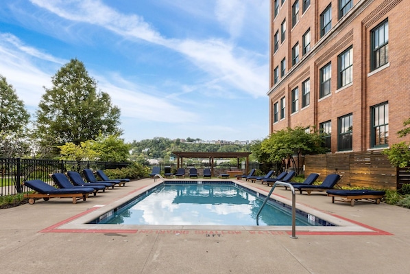 A rectangular pool with a red border, surrounded by lounge chairs and a brick building. - Historic Loft Retreat With Pool (Pittsburgh)