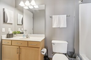 A modern bathroom with a white sink, wooden cabinets, a toilet, and a shower area. - Historic Loft Retreat With Pool (Pittsburgh)